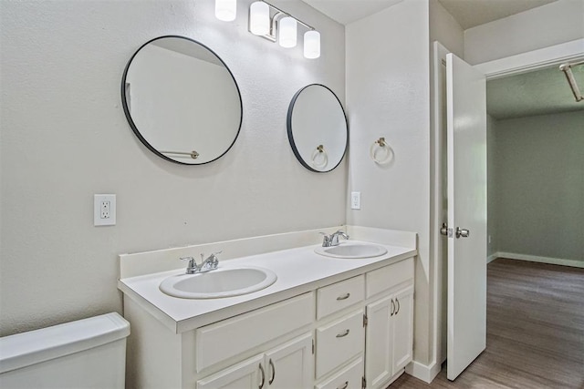 bathroom with toilet, wood finished floors, double vanity, and baseboards