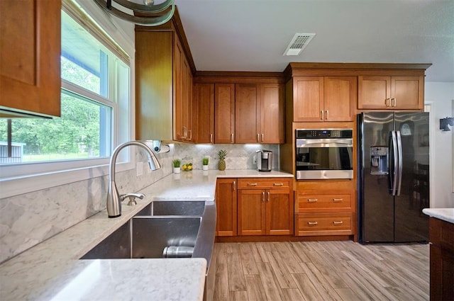 2590 Old 21 Rd, Idabel, OK 74745 - kitchen with stainless steel oven, black fridge with ice dispenser, a sink, brown cabinetry, and decorative backsplash