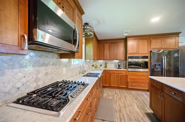 2590 Old 21 Rd, Idabel, OK 74745 - kitchen with stainless steel appliances, a sink, brown cabinets, decorative backsplash, and light wood-style flooring