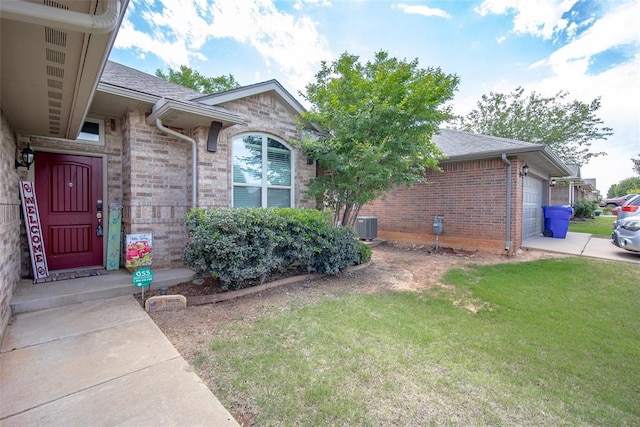 1528 Fawn Run Xing, Norman, OK 73071 - property entrance featuring brick siding, a lawn, central air condition unit, a garage, and roof with shingles