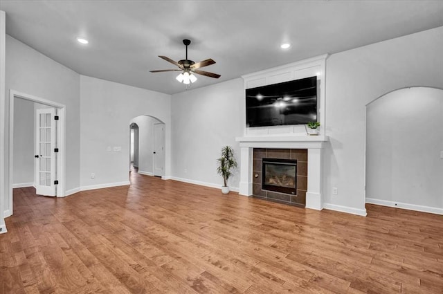 12824 NW 4th Ter, Yukon, OK 73099 - unfurnished living room featuring arched walkways, a ceiling fan, light wood-style flooring, a tiled fireplace, and recessed lighting