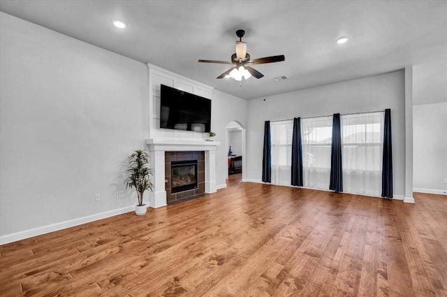 12824 NW 4th Ter, Yukon, OK 73099 - unfurnished living room with a ceiling fan, a tiled fireplace, light wood finished floors, recessed lighting, and arched walkways