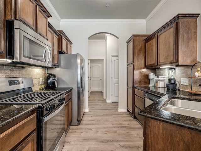 12005 NW 139th St, Piedmont, OK 73078 - kitchen with stainless steel appliances, dark stone counters, crown molding, light wood-style flooring, and arched walkways