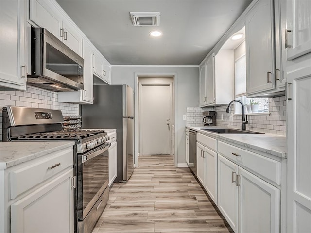 813 Branchwood Ct, Norman, OK 73072 - kitchen with stainless steel appliances, a sink, light wood-style flooring, backsplash, and white cabinets