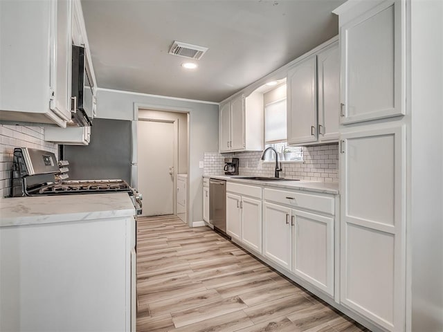 813 Branchwood Ct, Norman, OK 73072 - kitchen with a sink, stainless steel appliances, white cabinetry, light wood-style floors, and decorative backsplash