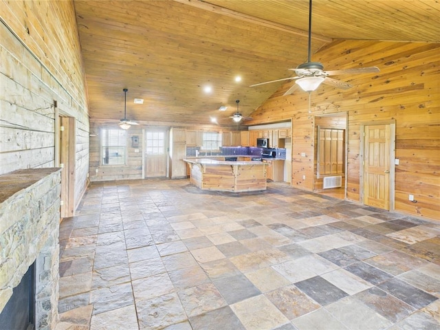 kitchen with ceiling fan, wood walls, stainless steel microwave, stone tile floors, and wooden ceiling