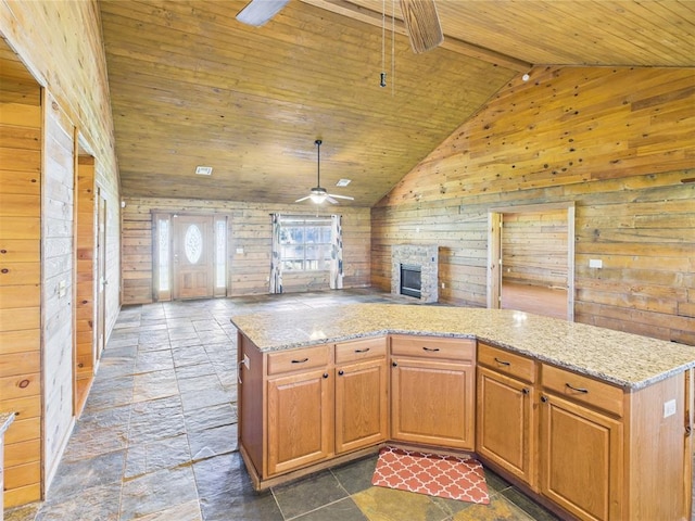 kitchen with wooden ceiling, a ceiling fan, wooden walls, open floor plan, and stone tile floors