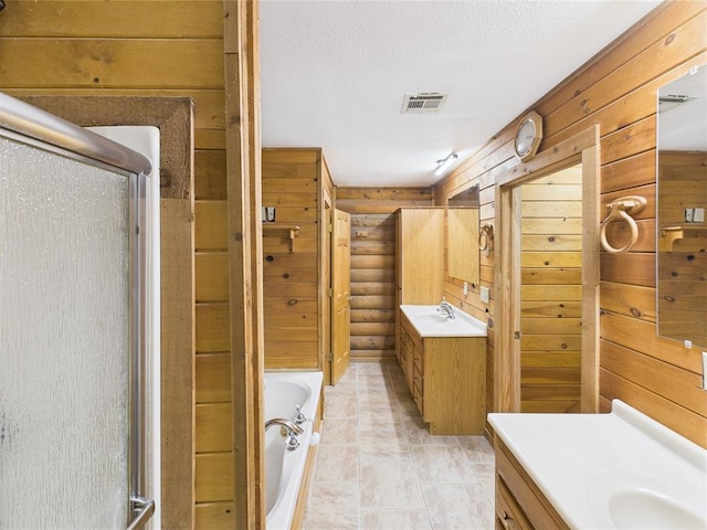 bathroom with two vanities, a stall shower, a garden tub, wood walls, and a textured ceiling