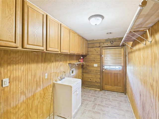 clothes washing area featuring hookup for a washing machine, stone finish floors, wood walls, and cabinet space