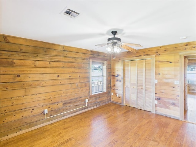unfurnished bedroom featuring wood walls, light wood-type flooring, a closet, and ceiling fan