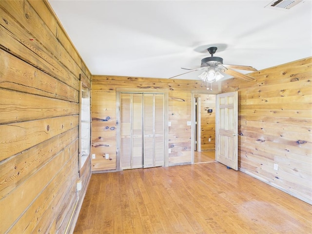 unfurnished bedroom with wood walls, light wood-style flooring, a closet, and ceiling fan