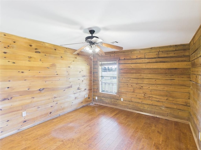empty room featuring hardwood / wood-style flooring, wood walls, and a ceiling fan