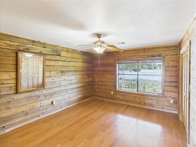 unfurnished room featuring a ceiling fan, wood walls, and light wood-style floors