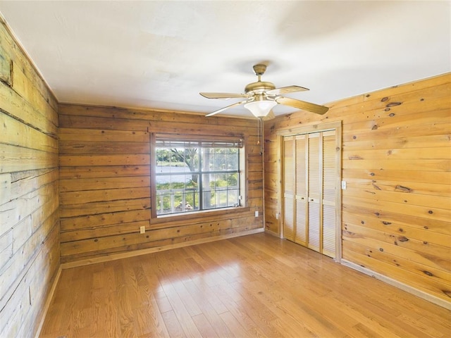 unfurnished bedroom with wood walls, light wood-style floors, a closet, and a ceiling fan
