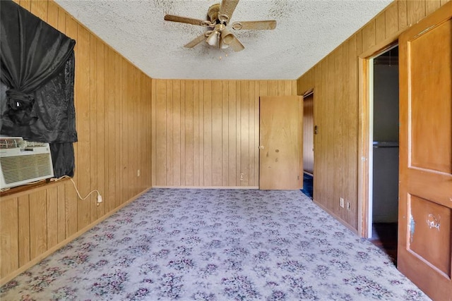 unfurnished room featuring wood walls, ceiling fan, a textured ceiling, baseboards, and carpet flooring