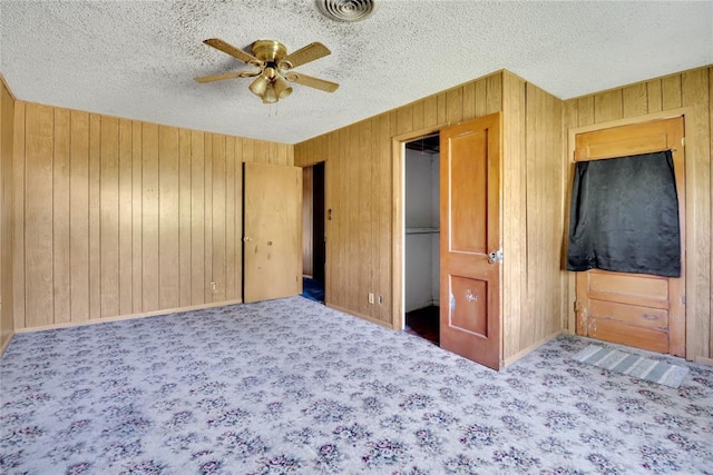 unfurnished bedroom with wooden walls, carpet floors, a textured ceiling, a ceiling fan, and baseboards