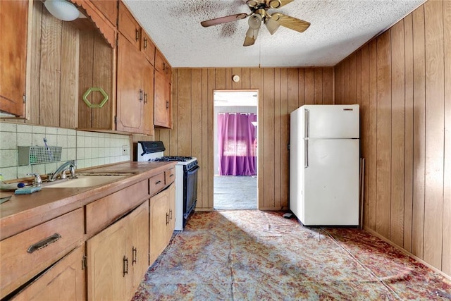 kitchen featuring freestanding refrigerator, range with gas stovetop, a textured ceiling, a ceiling fan, and wooden walls