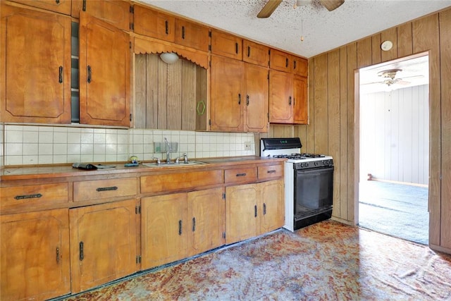 kitchen featuring range with gas cooktop, a ceiling fan, brown cabinetry, decorative backsplash, and a sink