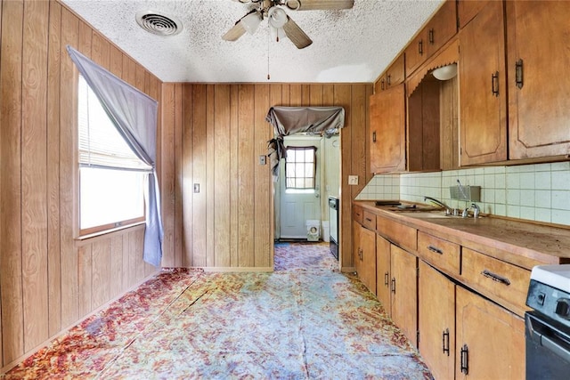 kitchen with tasteful backsplash, wooden walls, a sink, brown cabinets, and ceiling fan