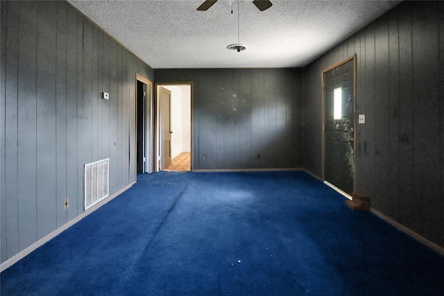 empty room featuring a ceiling fan, wood walls, carpet, and a textured ceiling