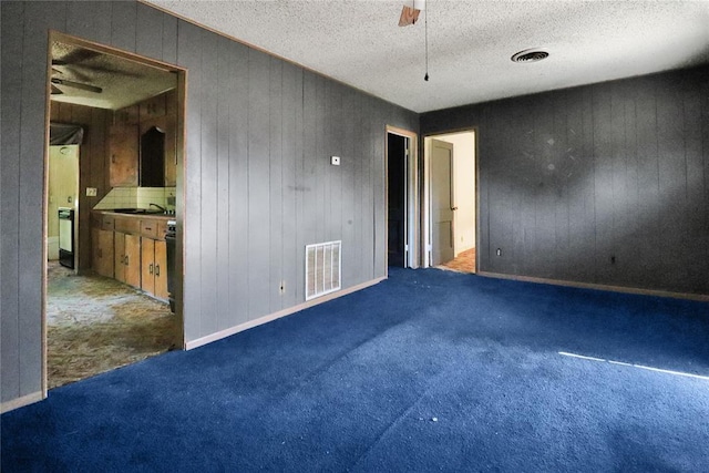 unfurnished room with a ceiling fan, wooden walls, carpet, a sink, and a textured ceiling
