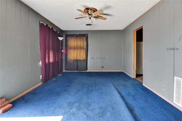 empty room featuring ceiling fan, carpet floors, a textured ceiling, baseboards, and wooden walls