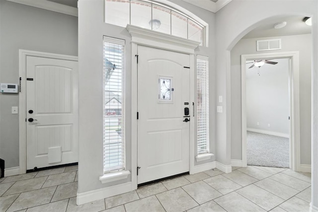 foyer entrance with light tile patterned flooring, arched walkways, ceiling fan, baseboards, and crown molding