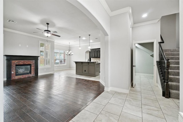 unfurnished living room featuring a ceiling fan, a brick fireplace, ornamental molding, arched walkways, and baseboards