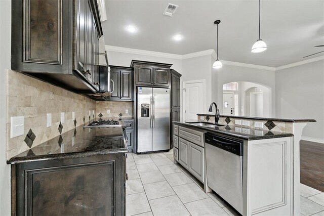 kitchen with appliances with stainless steel finishes, a sink, arched walkways, ornamental molding, and tasteful backsplash