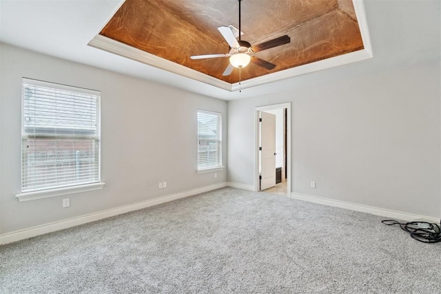 carpeted spare room with a tray ceiling, baseboards, and a ceiling fan