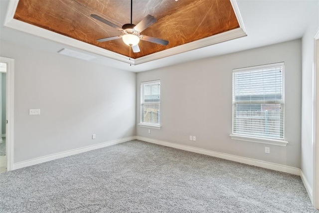 empty room with a tray ceiling, carpet flooring, a ceiling fan, and baseboards