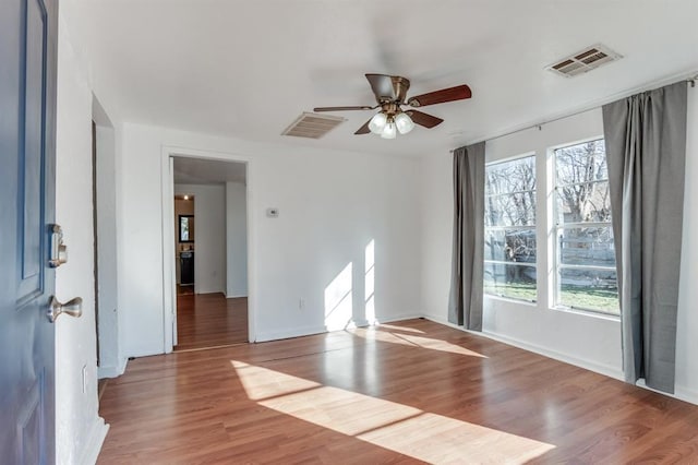 empty room with plenty of natural light, a ceiling fan, wood finished floors, and baseboards
