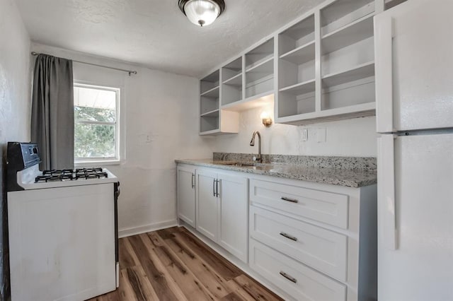 kitchen featuring white appliances, a sink, open shelves, wood finished floors, and light stone counters