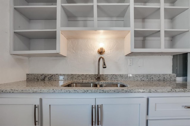 kitchen with open shelves, a sink, light stone counters, and white cabinetry