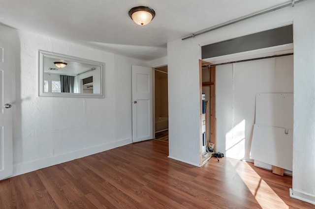unfurnished bedroom featuring wood finished floors, baseboards, and a closet