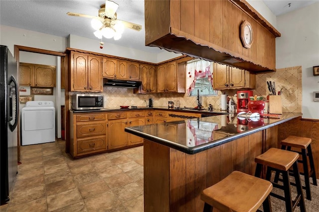 7108 S Kentucky St, Oklahoma City, OK 73159 - kitchen featuring stainless steel microwave, brown cabinetry, under cabinet range hood, a peninsula, and black refrigerator with ice dispenser