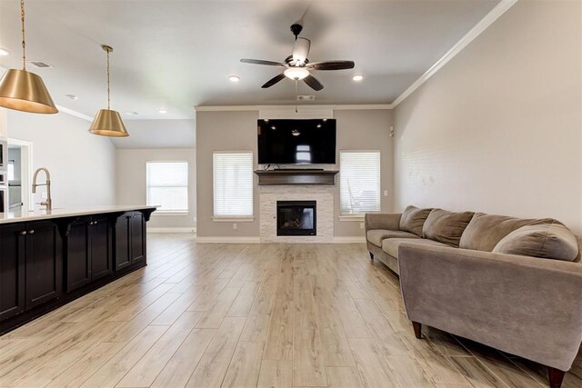 3024 Drake Crest Dr, Edmond, OK 73034 - living room with ceiling fan, crown molding, light wood-style flooring, a stone fireplace, and baseboards