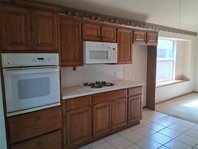 824 SE 38th St, Moore, OK 73129 - kitchen with white appliances, brown cabinetry, light countertops, light tile patterned flooring, and light colored carpet