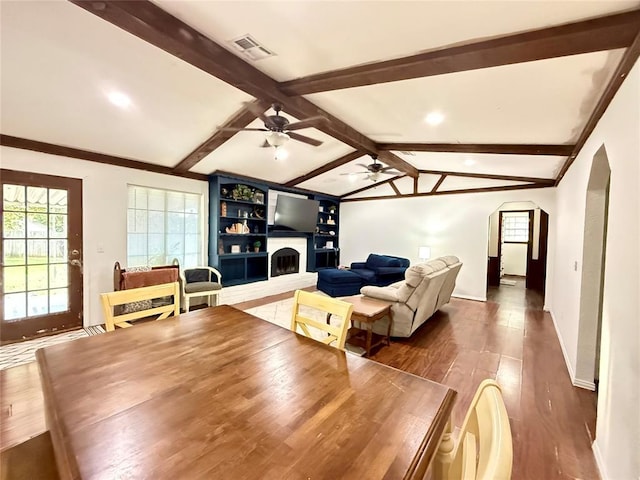 living area featuring a fireplace with raised hearth, arched walkways, dark wood-style flooring, ceiling fan, and baseboards