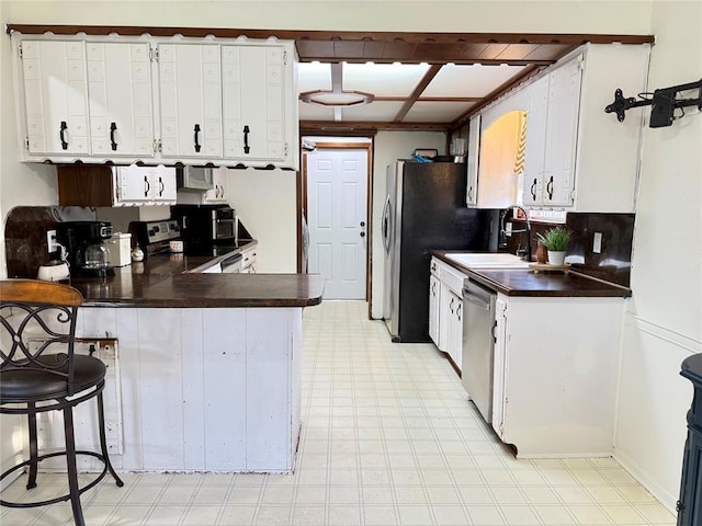 kitchen with a sink, dark countertops, appliances with stainless steel finishes, and a peninsula