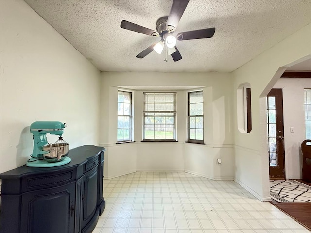 foyer with a textured ceiling, arched walkways, light flooring, a ceiling fan, and baseboards
