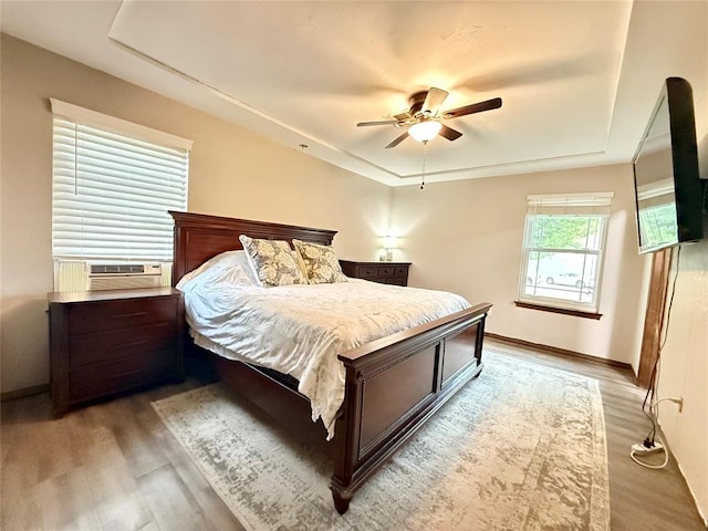 bedroom featuring a tray ceiling, wood finished floors, cooling unit, and baseboards