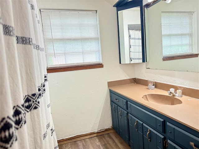full bath with wood finished floors, vanity, baseboards, and a textured wall