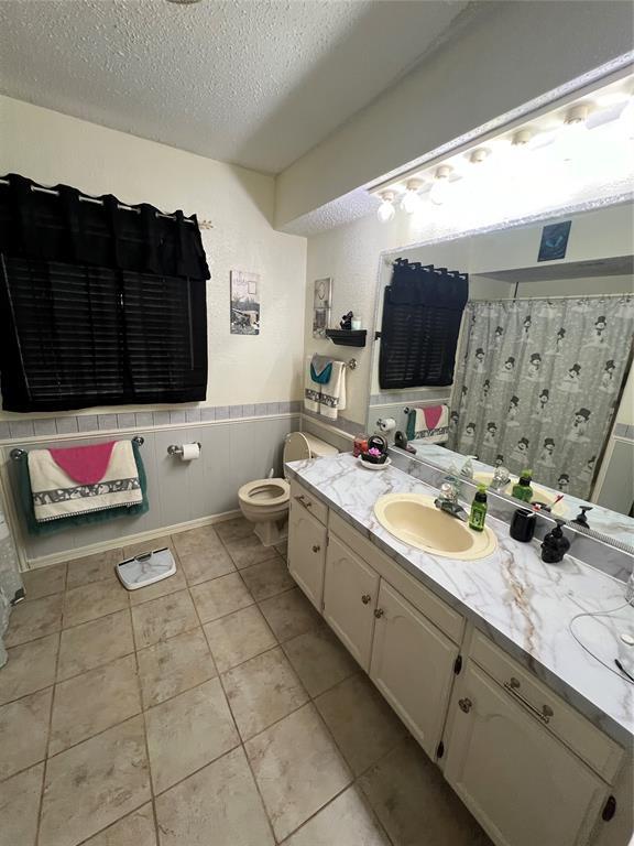 4125 Overland Dr, Del City, OK 73115 - full bathroom with a textured ceiling, toilet, a wainscoted wall, vanity, and tile patterned flooring
