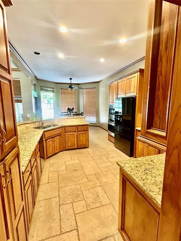 9817 Horseshoe Rd, Oklahoma City, OK 73162 - kitchen with recessed lighting, stone tile flooring, a sink, a peninsula, and brown cabinetry