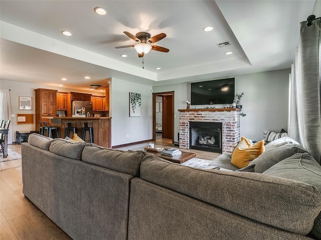 1015 N 3rd Ave, Stroud, OK 74079 - living area featuring light wood-style floors, a ceiling fan, recessed lighting, a tray ceiling, and a brick fireplace