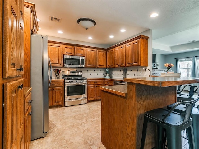 1015 N 3rd Ave, Stroud, OK 74079 - kitchen featuring stainless steel appliances, brown cabinetry, a kitchen breakfast bar, and recessed lighting