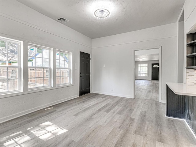 908 N Barta Ave, Prague, OK 74864 - unfurnished living room featuring light wood-type flooring, plenty of natural light, baseboards, and a textured ceiling