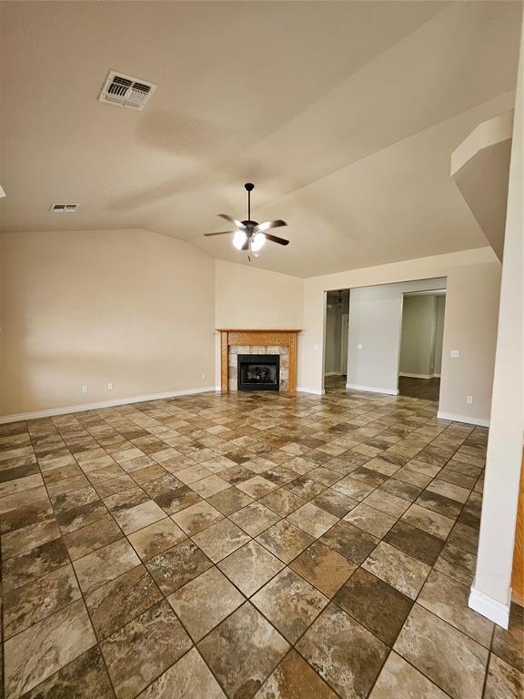 1801 Caribou St, Altus, OK 73521 - unfurnished living room with baseboards, ceiling fan, lofted ceiling, a tile fireplace, and dark stone finish flooring