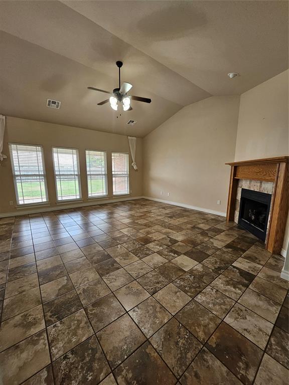 1801 Caribou St, Altus, OK 73521 - unfurnished living room with baseboards, ceiling fan, lofted ceiling, a tiled fireplace, and dark stone finish floors